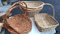 Side view of three large wicker baskets showing varied shapes and weave styles on white table outdoors