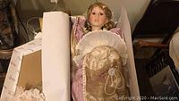 Porcelain Heirloom Doll Adele dressed in Victorian-style cream and pink dress with lace and pearls, lying inside original box with partial protective covering.