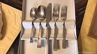 Photo showing a partial view of flatware pieces including spoons, forks, and a knife displayed inside a tray box.