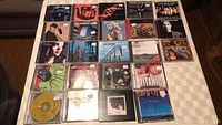 Overview photo showing 23 music CDs arranged on a surface, mixed artists and genres.