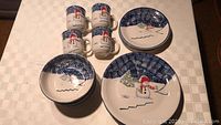 Photo of four place settings of dishes with snowman winter design, showing dinner plates, salad plates, bowls and mugs white ceramic with blue and snowman artwork