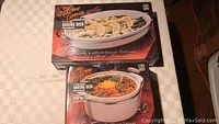 Box of oval 9x13 inch ceramic and metal baking dish with food image on box front showing casserole.