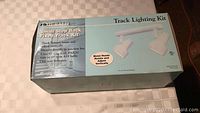 Light blue box labeled Emerald Small Step Back Fixed Track Lighting Kit with images of two white track lighting heads that rotate and adjust vertically.