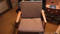 Front view of wooden armchair with solid brown woven cushion on seat and backrest.