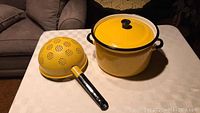 Bright yellow porcelain pot with lid and matching colander on table.