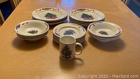 Dinner plates, soup or pasta bowls, salad plates, and a coffee mug displayed on a table showing the Christmas tree design with ribbons and holly.