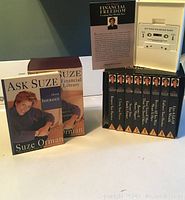 Set of 9 Suze Orman Financial Freedom audio cassettes in cases next to 7 Ask Suze Financial Library softcover books.