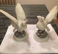 Front angle view showing two porcelain white dove figurines on cloth.