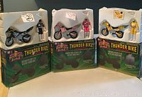 Image of three boxed Power Rangers Thunder Bikes with corresponding action figures: Black Ranger with black bike, Pink Ranger with pink bike, Yellow Ranger with yellow bike.