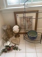 Overview of lot items including framed print, towel rack, mirror, ceramic bowl, cherub figurine, heart-shaped decor, floral arrangement, and votive holder on tiled floor.