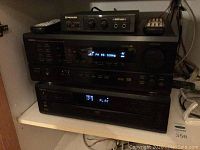 Denon AVR-1801, DVM-1800 and Pioneer Karaoke mixer MA-3 units visible on a shelf showing front panel displays and controls of each device.
