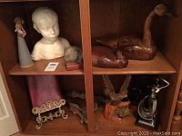 Photo showing upper shelves of cabinet containing child's bust, woman and child figurine, wood carved goose and duck.
