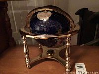 Globe showing dark blue oceans and a white Antarctic region, mounted on a shiny brass stand with three legs and a brass meridian.