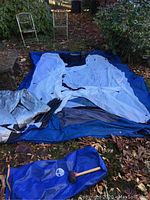 Overview of three folded tents laid on blue tarp with tent poles and carry bag with mallet.