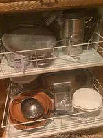 Drawer of stainless steel pots and pans, terracotta pans, kitchen utensils including a metal ladle and grater.