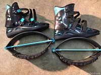 Side view of Kangoo Jumps rebound boots showing black shell with turquoise adjustable straps and curved spring frame base for rebounding fitness activity.