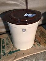 Full view of the light cream-colored stoneware crock with brown lid on top, showing shape and condition.