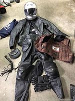 Full gear laid out on concrete: helmet, helmet bag, jacket, liner, pants, gloves, balaclava, pouch