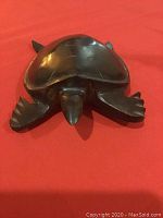 Single medium-sized dark polished wooden turtle sculpture with carved shell and limbs, displayed on red fabric background.