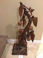 Full view of wooden sculpture showing man climbing tree with leaves and fruit