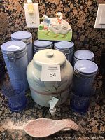 Photo showing the small water dispenser, six light blue canisters, two matching glasses, utensil holder with duck design, and pink ceramic spoon rest on a kitchen counter.