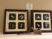 Frontal photo showing two wood and gold-tone framed sterling silver charm sets mounted on black background, with a brass frog figurine placed in front.