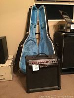 Crate amplifier in front of open guitar case showing blue plush interior