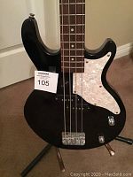 Close-up of bass guitar body showing black finish, white pearloid pickguard, pickups, bridge and control knobs.