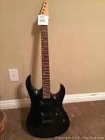 Front view of black electric guitar body and neck without strings, headstock has tag number 108.