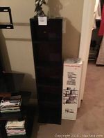 Photo showing the tall black multimedia shelving unit with multiple shelves alongside its packaging box.