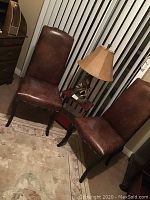 Two brown leather-look chairs with studded edges, positioned near a window and a carpeted floor.