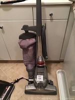 Front view of Kirby Sentria upright vacuum cleaner with cloth bag and power cord wrapped on side hooks, grey and silver color.