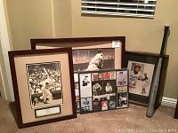 Photo showing framed prints of Mickey Mantle batting, Joe DiMaggio sliding into third base, framed Roberto Clemente photo, and a vintage wooden baseball bat leaning against the wall.