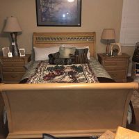 Full front view of queen bed with nightstands on each side, lamps on nightstands, bedsheets, comforter, decorative pillows and Santa themed throw blanket at foot of bed.