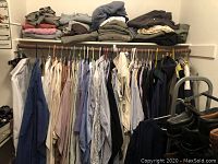 Photo of men's button-up shirts hung on wooden and metal hangers, folded clothes on a shelf above.