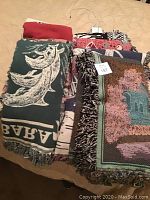 Pile of colorful woven cotton blankets with different patterns including a green one with a large leaf design and fringed edges.