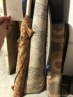 Rolled beige and burgundy upholstery fabric and two rolled rugs.