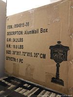 Cardboard shipping box with item number, weight, dimensions, and a black printed outline image of the mailbox on pedestal stand.