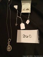 Photo of all items in the lot: rhinestone pendant necklace, rhinestone cross necklace, two sterling silver rings in box.