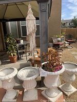 Photo of four white decorative plant urns on square pedestals, one with succulent and small pink flowers, outdoor patio setting.