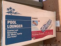 Photo of the original packaging box for a Poolmaster Pool Lounger. Box states 'Comfort and Relaxation the Whole Family Can Enjoy', features palm tree and beach graphics, photo of the product in use showing a woman reclining on the lounger with the blue currents pattern.