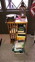 Small wooden table next to a window holding a wooden lantern and cloth, with books stacked on and under the shelves