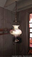 Full view of hanging lamp showing brass base, floral glass globe, and hanging chain.