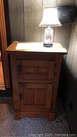 Full view of wooden cabinet with closed doors and ceramic floral lamp on top