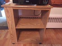 Photo showing the front and side of the wooden kitchen cart with three shelves and caster wheels, top surface holding a microwave (not included)