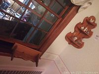 Two wooden wall-mounted corner shelves mounted on wall with various ceramic and glass knick-knacks displayed.