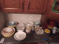 Overview of entire lot on countertop showing mixing bowls, bakeware, CorningWare pieces, serveware and storage items