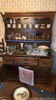Full view of wooden hutch with open shelves displaying cups and glasses, bottom cabinet with drawers and doors.