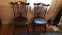 Two wooden side chairs with spindle backs and turned legs. Dark brown finish with visible wear and scratches.