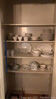 Shelf holding white swirl patterned plates, bowls, saucers, ceramic mugs, and clear drinking glasses, also small dishes and serving bowls